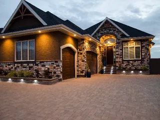 Paver driveway and stone-front house at dusk